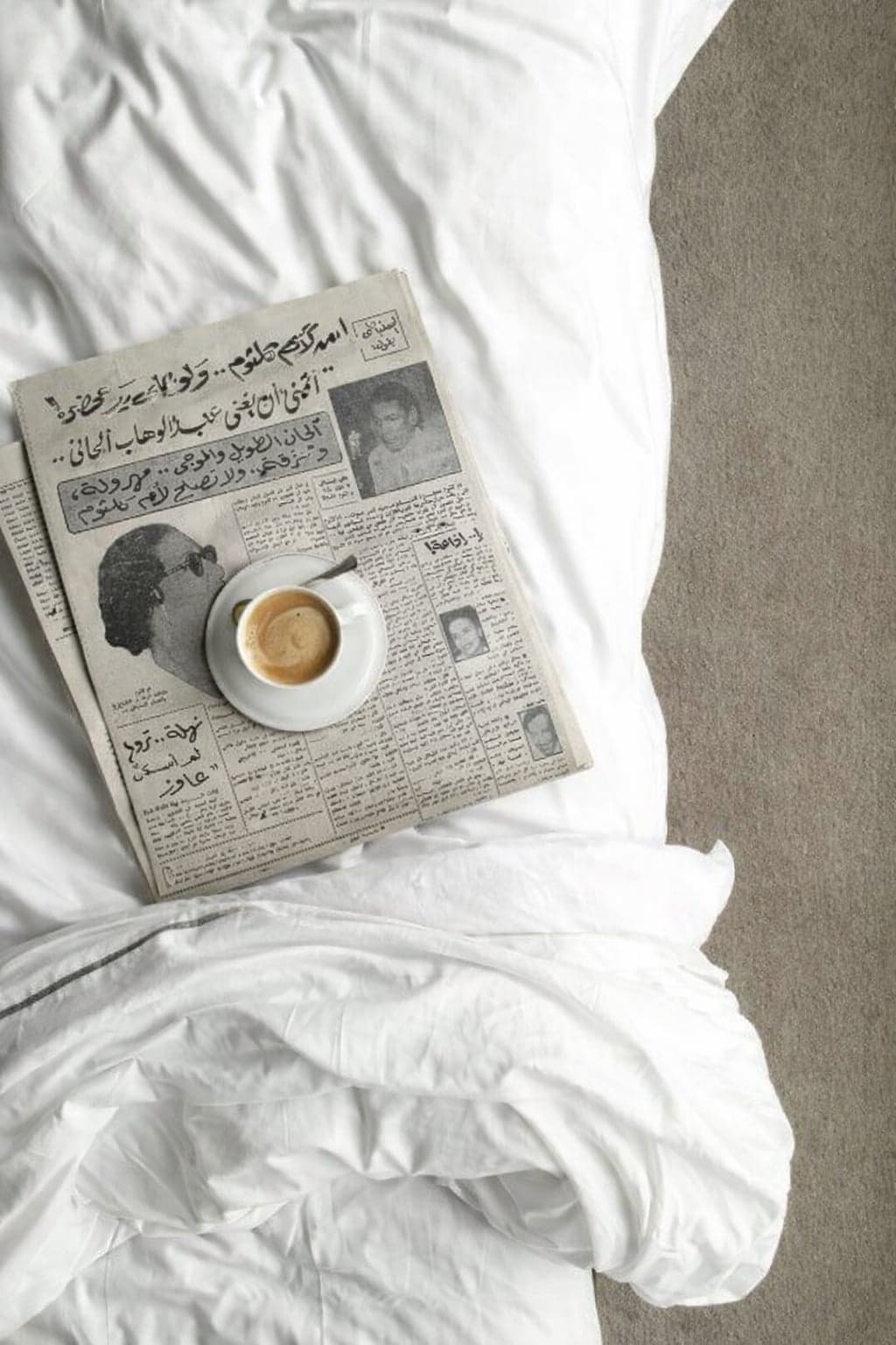An Arabic newspaper and a cup of coffee on white bed linen