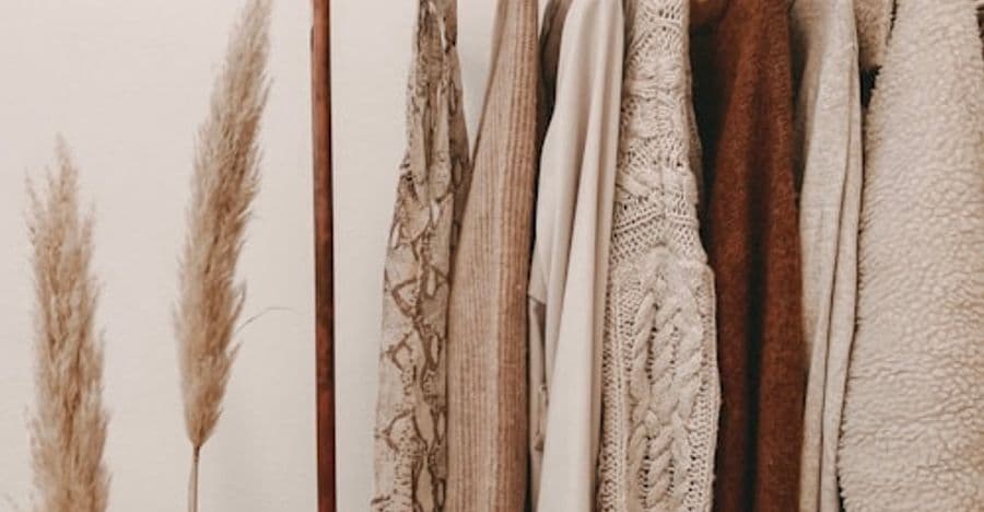 Knitwear in neutral tones on a rail beside dried pampas grass.