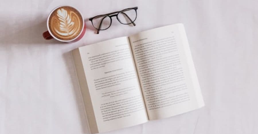 كتاب مفتوح ونظارة قراءة وفنجان لاتيه على قماش أبيض.