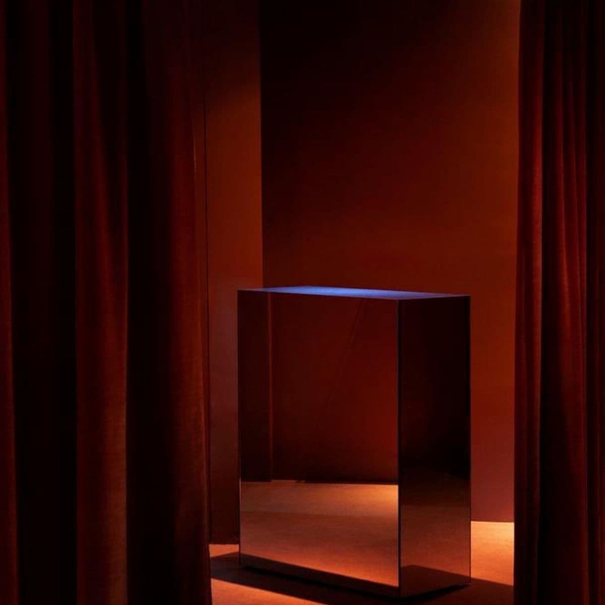 A red-curtained salon lit by a single lamp